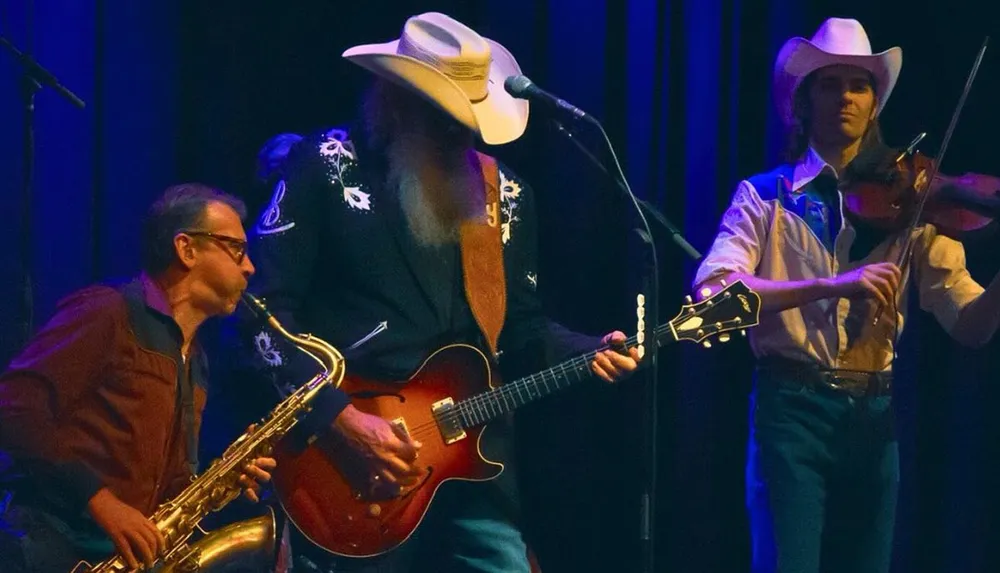 Three musicians perform on stage one playing saxophone another electric guitar and the third playing violin all wearing cowboy hats