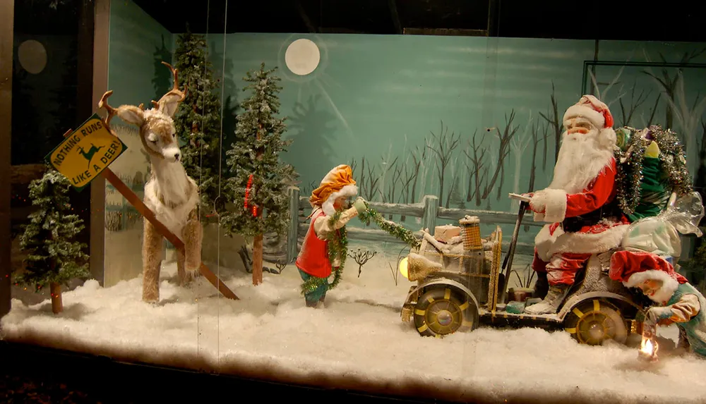 The image shows a whimsical holiday display with a mechanical Santa and his helper elf on a snow-covered lawn featuring a reindeer and humorous signage