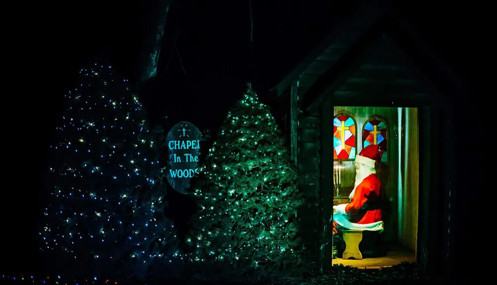A person dressed as Santa Claus is humorously depicted sitting on a toilet inside a small building adorned with Christmas lights and a sign Chapel In The Woods