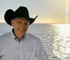 A person wearing a cowboy hat is standing in front of a body of water during a bright sunny day