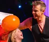 A man is playfully rubbing an orange balloon on a laughing girls head likely creating static electricity