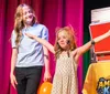 A man is playfully rubbing an orange balloon on a laughing girls head likely creating static electricity