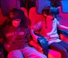 Several people are seated in red-lit chairs wearing virtual reality headsets appearing engaged and animated