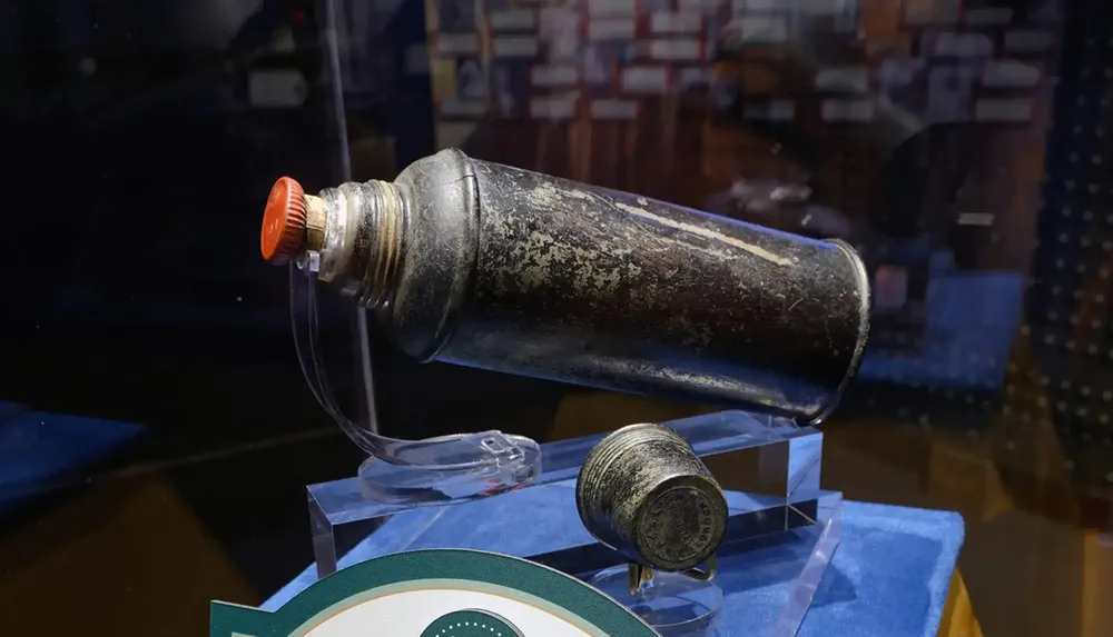 A vintage metal container with a red cap is displayed on a stand likely in a museum setting