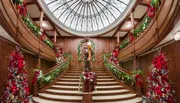 A grand staircase is ornately decorated with festive greenery, red ribbons, and lights, beneath a large dome ceiling.