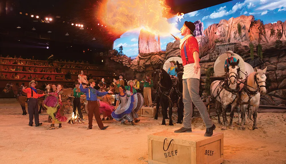Performers in Western attire are entertaining an audience with a fire-breathing act surrounded by horses and vibrant costumes in a lively show setting