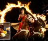 A performer rides two horses through a flaming ring in a dramatic lit-up setting