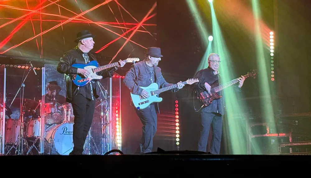 A band is performing live on stage with two guitarists a bassist and a drummer under colorful lights
