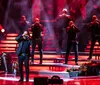 A group of performers is singing passionately on a dramatically lit stage accompanied by red lighting and stage smoke