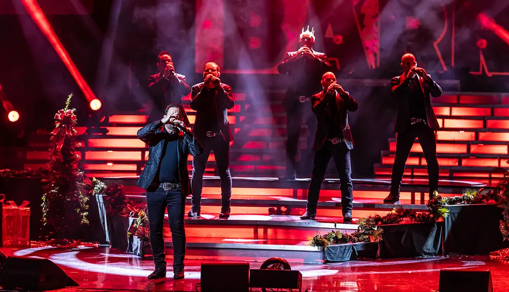 A group of performers is singing passionately on a dramatically lit stage accompanied by red lighting and stage smoke