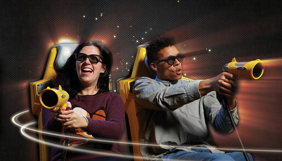 Two people wearing 3D glasses are enthusiastically playing an interactive game with toy guns in a dynamic setting.