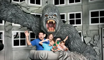 A family poses playfully with a giant gorilla statue that appears to be roaring and grabbing them.