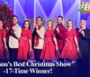 A group of performers in festive attire is on stage in a Christmas-themed show with a backdrop of falling snow