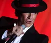 A performer in a black hat and suit is singing into a microphone against a red background