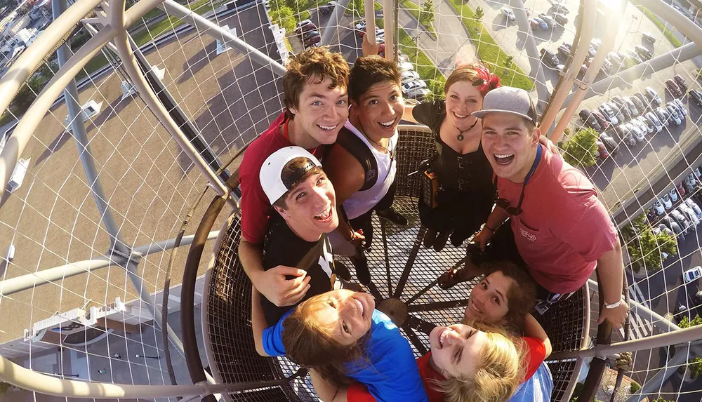A group of joyful friends takes a selfie from a high vantage point on a sunny day with their faces close together and a parking lot visible below