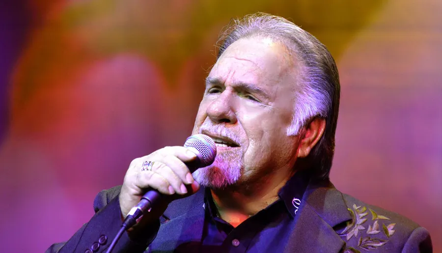 A man is passionately singing into a microphone on a colorful stage.