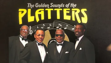 Four men in tuxedos stand in front of a backdrop featuring the phrase 