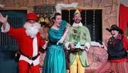 Four people are dressed in colorful and theatrical Christmas-themed costumes, expressing exaggerated emotions in what appears to be a festive play or performance.