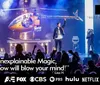 The image shows a staged performance featuring a helicopter and performers under dramatic lighting with a quote praising the shows magic and logos from various media outlets including MTV Hulu and Netflix