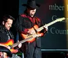 Three musicians are performing on stage with two playing guitars and one playing a harmonica