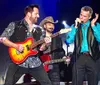 Three musicians are performing on stage with two playing guitars and one playing a harmonica