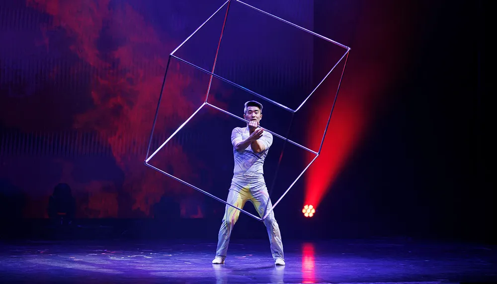 A performer manipulates a large wireframe cube on stage surrounded by dramatic lighting