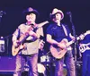 Three musicians stand confidently in front of a vintage blue pickup truck holding their guitars exuding a classic Americana vibe