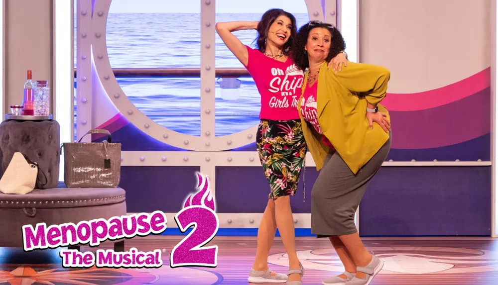 Two women pose playfully on stage in front of a backdrop resembling a ships interior promoting Menopause The Musical 2