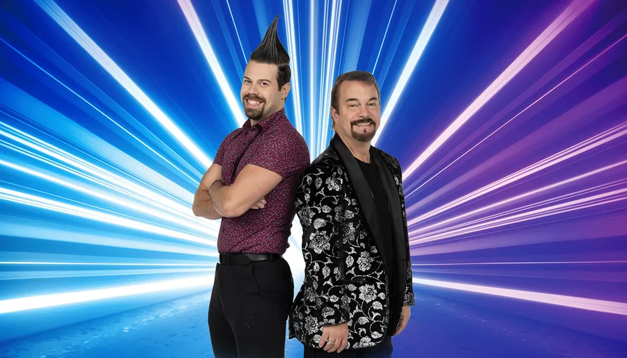 Two smiling men with distinctive hairstyles stand back-to-back against a vibrant blue background with dynamic white light streaks.