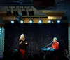 A musician is performing on stage singing into a microphone while playing a Roland RD-700 keyboard set against a backdrop of sparkly blue curtains and decorative panels