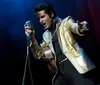 A person dressed in an elaborate gold and black outfit performs with a guitar and a vintage microphone exuding a strong stage presence reminiscent of classic rock and roll