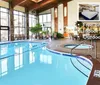 The image shows an inviting indoor pool area with wooden beams stone accents and lounge chairs featuring text about amenities like free breakfast an indoor pool and an outdoor pool