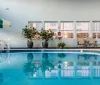The image shows an indoor swimming pool with patio furniture and potted plants creating a serene leisurely ambiance