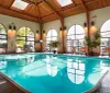 This image features an indoor swimming pool with a vaulted ceiling large arched windows and multiple seating areas