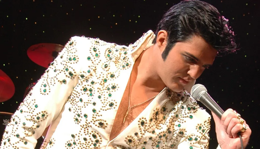 A performer in a bejeweled white suit is singing into a microphone on stage