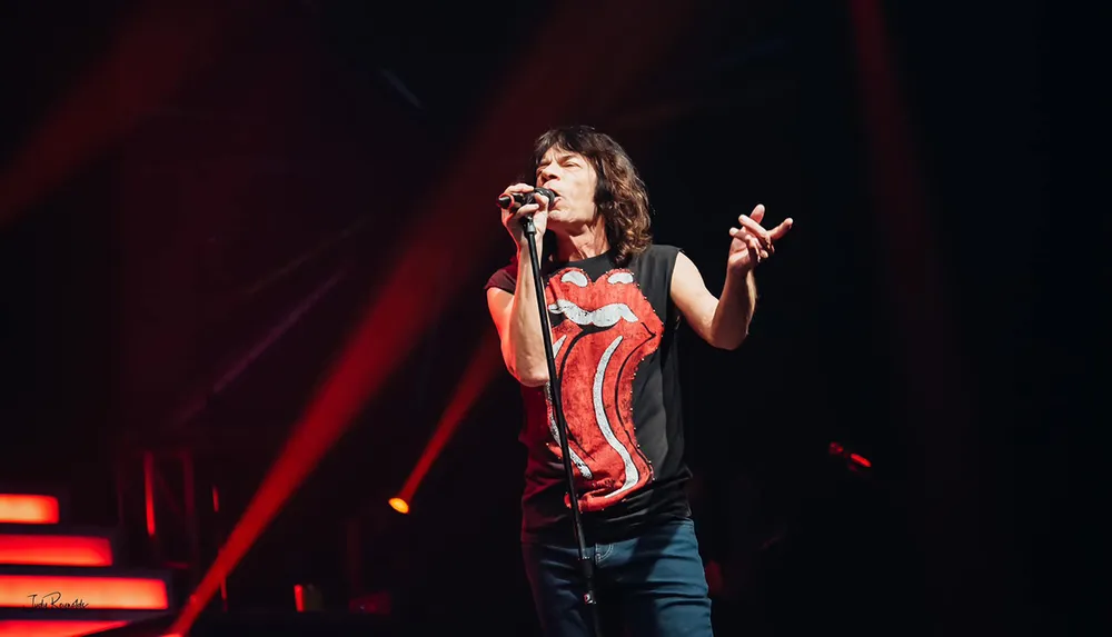 A person sings passionately on stage wearing a Rolling Stones T-shirt with red spotlights illuminating the scene