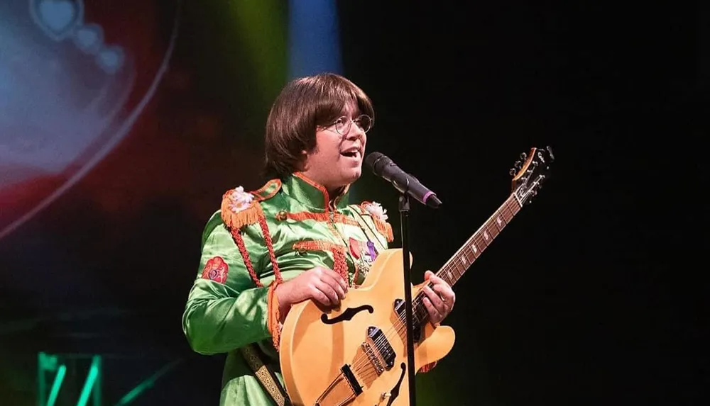 A musician dressed in a colorful vintage-style costume is performing on stage with a guitar