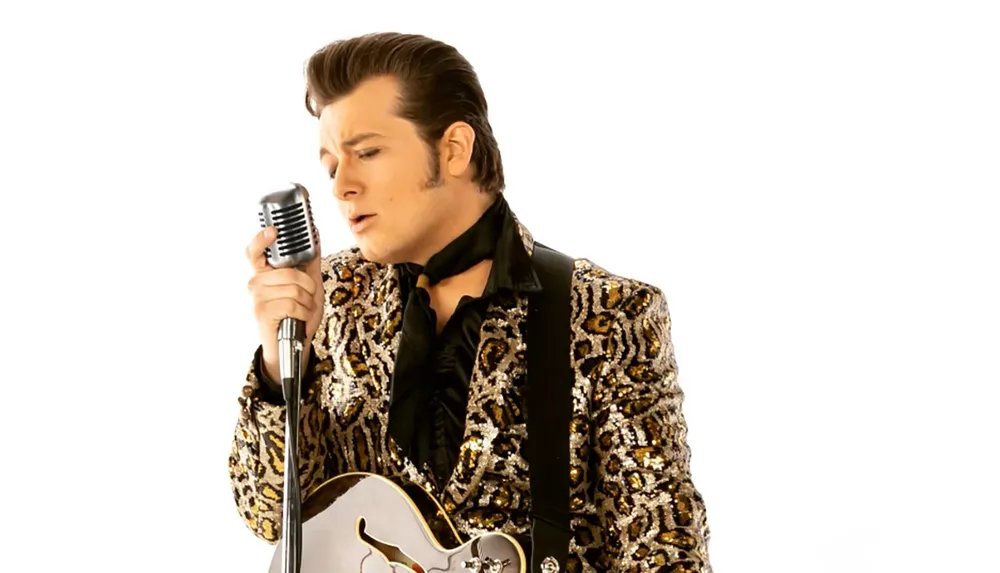 A person dressed in a leopard-print jacket sings into a vintage microphone while holding a guitar