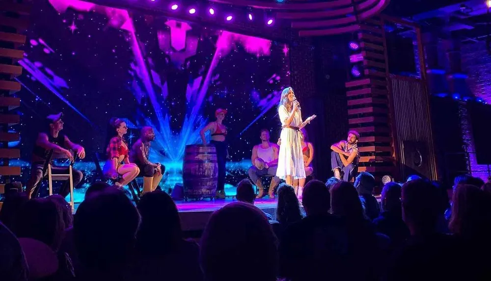 A performer is singing on stage accompanied by musicians with an audience watching under purple and blue stage lighting