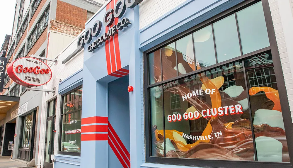 The image shows the exterior of the Goo Goo Chocolate Co advertising itself as the home of the Goo Goo Cluster with a colorful storefront and signage in an urban setting