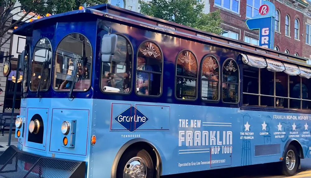A blue trolley-style tour bus operated by Gray Line is parked on a city street advertising The New Franklin Hop Tour in Tennessee