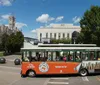 An orange and green trolley bus with the label Old Town Trolley Tours is driving past a row of historic buildings on a sunny day