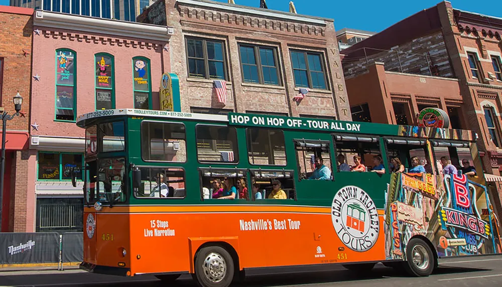 An orange and green trolley bus with the label Old Town Trolley Tours is driving past a row of historic buildings on a sunny day