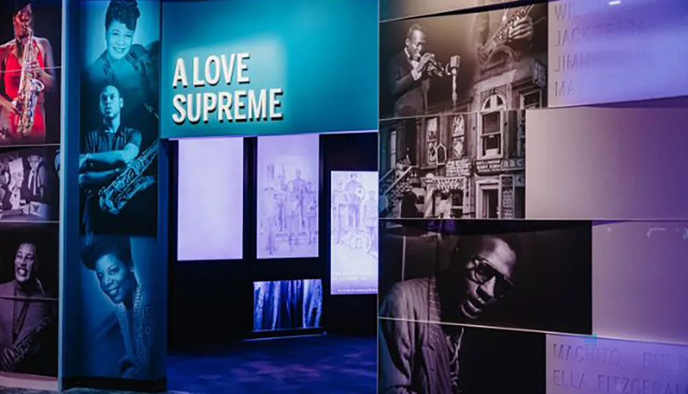 The image shows an exhibition space with illuminated photos and graphics of jazz musicians accompanied by the title A LOVE SUPREME in bold lettering
