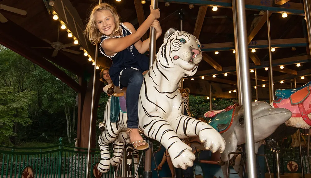 A joyful child is riding a white tiger on a carousel adorned with lights