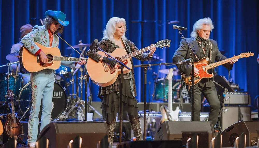 Three musicians perform on stage playing acoustic and electric guitars flanked by various instruments and amplification equipment