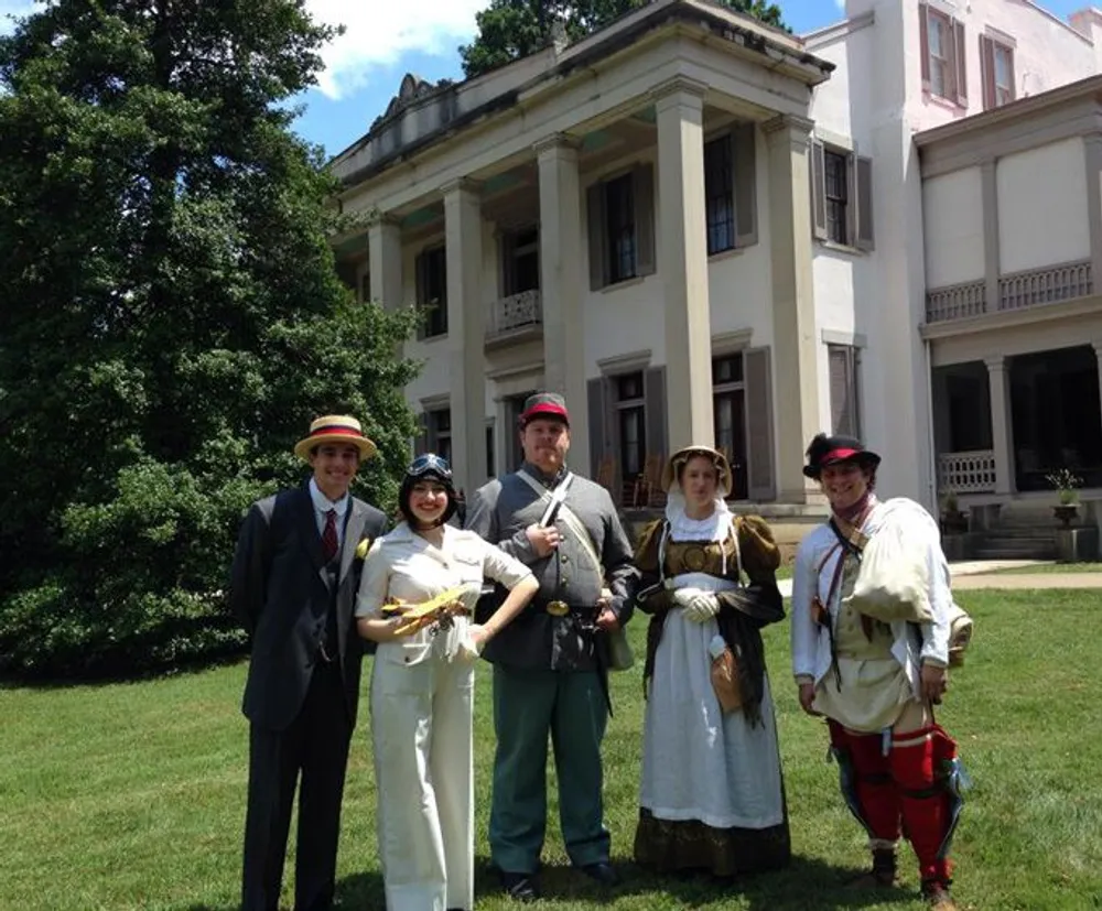 People in various historical costumes are posing in front of a stately building on a sunny day