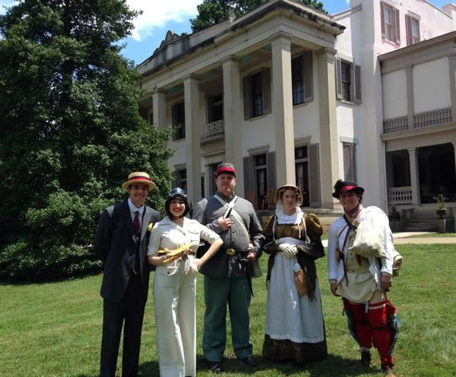 People in various historical costumes are posing in front of a stately building on a sunny day.