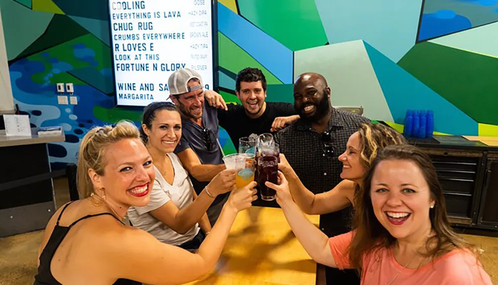 A group of cheerful people are toasting with drinks at a bar or event with a colorful geometric background