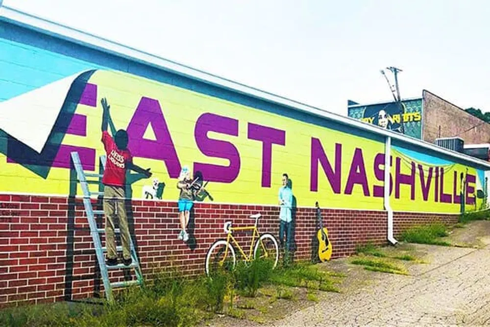 People are painting a colorful mural that says EAST NASHVILLE on the side of a building